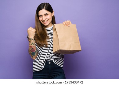 Thrilled Young Woman Happy To Receive Her Takeout Food For Lunch. Hispanic Woman Smiling And Holding A Brown Bag With Delivery Food