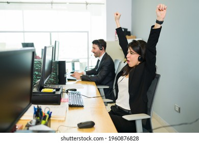 Thrilled Young Woman Raising Her Arms And Shouting With Happiness While Sitting At Her Desk In A Call Center. Sales Representative Winning A Big Sale Deal