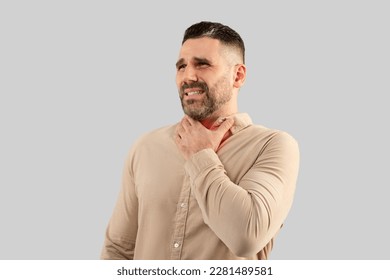 Throat pain. Portrait of ill businessman touching his neck, suffering sore throat, viral infection or flu symptoms, posing on light grey studio background - Powered by Shutterstock