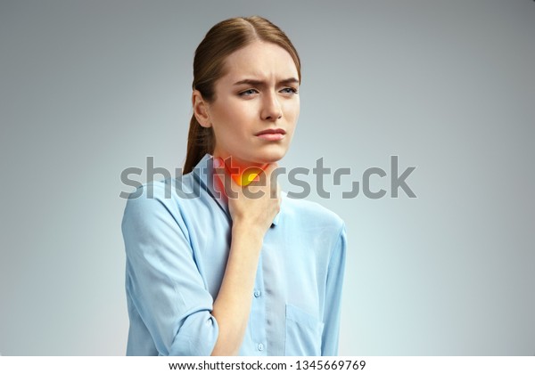 Throat\
pain. Woman holding her inflamed throat. Photo of american woman in\
blue shirt on gray background. Medical\
concept