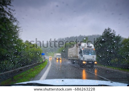 Through the car's windshield view on the highway and oncoming traffic in a storm. Drops of water on the glass. Image in the art defocus. Left-hand traffic