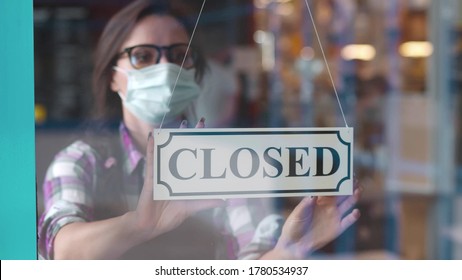 Through glass view of female business owner in safety mask hanging up sign with inscription closed on cafe door. Waitress in protective mask closing restaurant because of pandemic