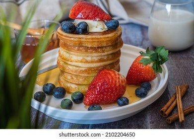 Through The Grass View Of Stack Of Pancakes With Honey Stick, Strawberry, Blue Berry And Whip Cream On Top In Plate, Delicious Dessert With Milk For Breakfast.