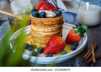 Through The Grass View Of Stack Of Pancakes With Honey Stick, Strawberry, Blue Berry And Whip Cream On Top In Plate, Delicious Dessert With Milk For Breakfast.