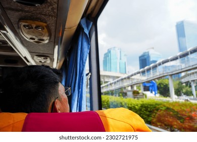 Through the window of a moving bus, a man takes in the awe-inspiring view of towering skyscrapers and the vibrant cityscape below