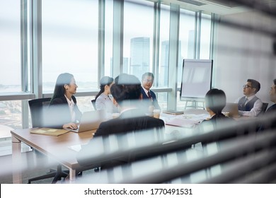 Through-the-glass Shot Of A Team Of Asian Business People Meeting In Company Conference Room