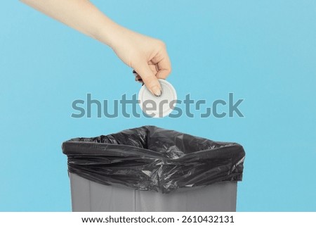 throw a cap from a plastic bottle into the trash bin, hold a cap from a plastic bottle in your hand in front of a trash can, plastic recycling concept