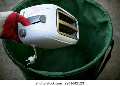 Throw old household appliances in the trash.A hand throws a sandwich toaster into a bucket.Disposal of kitchen appliances.