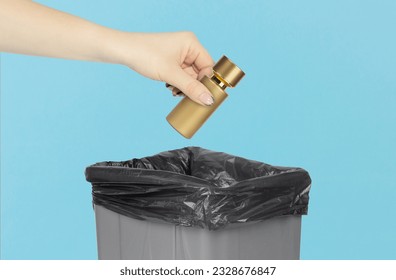 Throw Perfume bottle in trash can, Perfume bottle in hand in front of trash can, concept of bad aroma, glass recycling, gray trash can on blue background