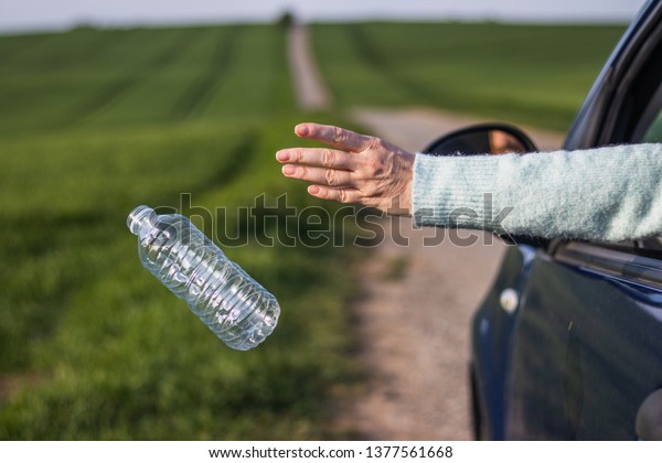 Throwing away plastic bottle\
from car. Driver throwing garbage on road. Environmental\
conservation