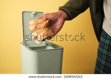 Throwing bread slices into a trash bin on yellow backdrop