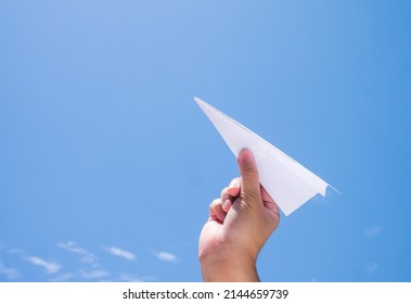 throwing paper plane to the sky, human's hand holding paper craft against blue sky background
