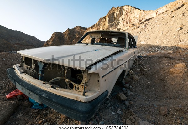 The thrown skeleton of the car lies in the\
midst of rocky mountains near the\
coast