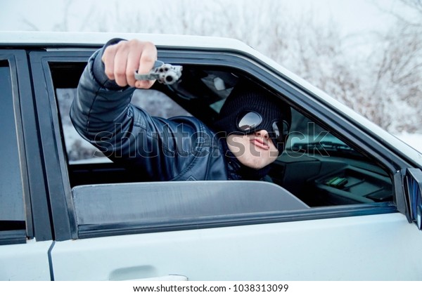 thug in the car on the road with a gun in his\
hands. robber on the road. a terrorist in a black mask threatens\
the driver on the road.
