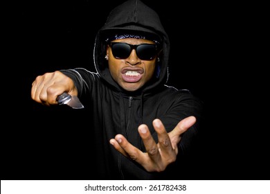 thug wearing a hoodie and holding a knife coming out of the shadows