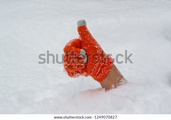 Thumb up in orange glove protruding out from under\
the snow.