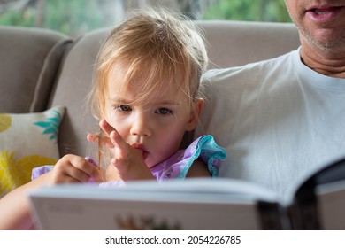 Thumb Sucking. A Little Girl Reading A Book With Her Dad.