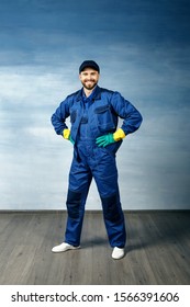 Thumb up. Young handsome man with a beard in a blue working uniform for cleaning rooms smiles isolated on blue background,