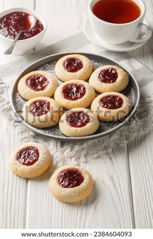 Thumbprint Christmas cookies filled with raspberry jam closeup on the plate served with tea on the white wooden table. Vertical
