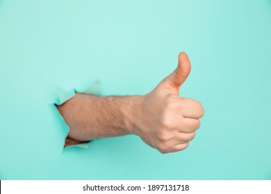 Thumbs up through the hole in blue paper sheet