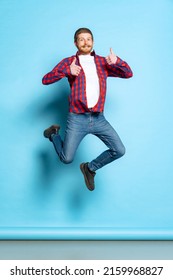 Thumbs up  Emotional young red  headed man in white t  shirt   plaid shirt jumping isolated blue background  Concept art  fashion  emotions  aspiration  Copy space for ad