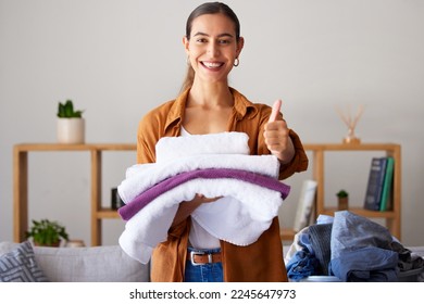 Thumbs up, laundry and portrait of a woman maid folding clothes in the living room in a modern house. Happy, smile and female cleaner or housewife with a thumbsup cleaning or doing chores in a home.