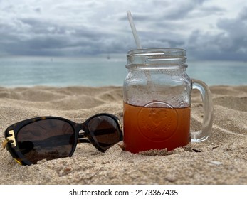 Thunder Bay, Barbados - May 25, 2022: A Glass Mason Jar With A Straw Filled With Rum Punch And Sunglasses On A Beach With Dramatic Clouds In The Background