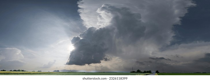 A thundercloud in a dramatic cloudy sky passes over agricultural land with its wispy clouds