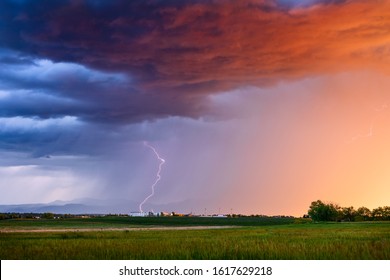 Thunderstorm with lightning bolt and dramatic storm clouds over a field at sunset