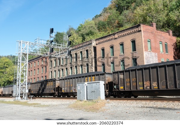Thurmond,\
West Virginia US - October  10,  2021: Traffic signal high above\
tracks  with historic buildings behind loaded coal train cars ready\
to depart to  power plant destination \
delivery
