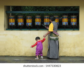 Tibetan mother and her child spinning Prayer wheels in Dharamsala, India. 
Text on  Prayer wheels : "Om Mani Padme Hum" :  the 6 syllables in relation to suffering (famous mantra in Buddhism)