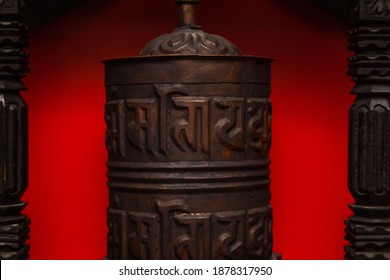 Tibetan prayer drum made of copper on a red background. The cylinder on the axis contains the mantra. Image of the mantric inscriptions of Avalokiteshvara "om mani padme hum" on the prayer drum.