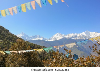 Tibetan prayer flags among trees with Meili Xue Shan mountain range on the background in Deqin town, Yunnan province, China. Freedom symbol, nature landscape concepts