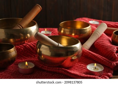 Tibetan singing bowls with mallets and burning candles on red fabric