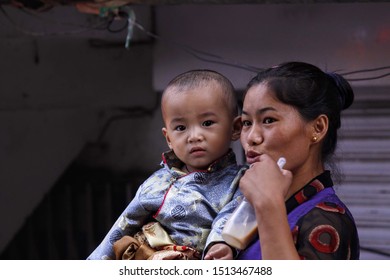 A Tibetan woman carrying her baby boy wearing traditional Tibetan dress. The baby boy is seen looking straight at the camera. Shot in Dharamshala India May 2012