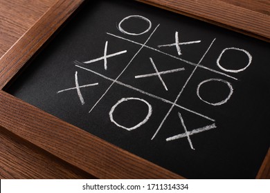 Tic Tac Toe Game On Blackboard With Chalk Grid, Naughts And Crosses On Wooden Surface