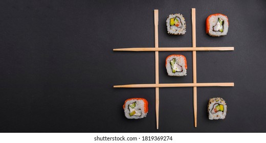 Tic tac toe game with sushi on dark black background, creative concept sushi rolls. Banner, playing tic tac toe game. Japanese cuisine concept, sushi advertisement.