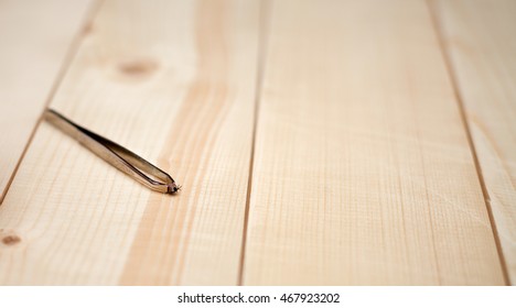 Tick On Tweezers On Wooden Background