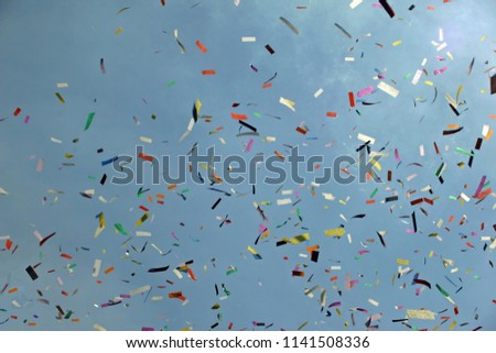 Ticker tape released at an event shown against a blue sky with flare from the sun in the corner.