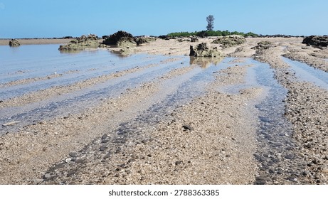 Tidal patterns etched into the sandy seabed with small rock formations and distant lighthouse