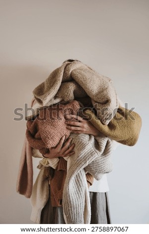 Tidy Stack Of Knitted Woolen Jumpers In Neutral Palette Held By A Woman