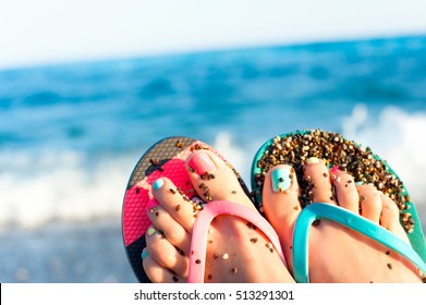 Tidy Woman Feet With Multi-colored Pedicure In Slippers On Summer Pebble Beach. Vibrant Outdoors Horizontal Inspirational Close-up Image With Blue Seascape Background.