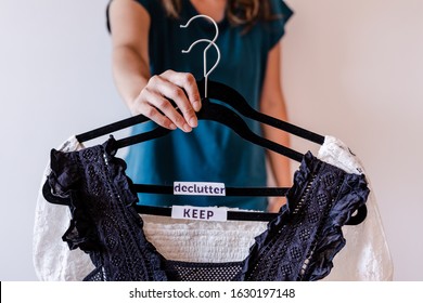 tidying up and decluttering conceptual still-life, woman holding clothes hangers with black and white tops and text labels to sort between items to Keep and Declutter shot at shallow depth of field