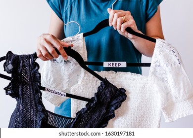 Tidying Up And Decluttering Conceptual Still-life, Woman Holding Clothes Hangers With Black And White Tops And Text Labels To Sort Between Items To Keep And Declutter Shot At Shallow Depth Of Field