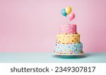 Tiered birthday cake with pastel colored tiers decorated with party balloons