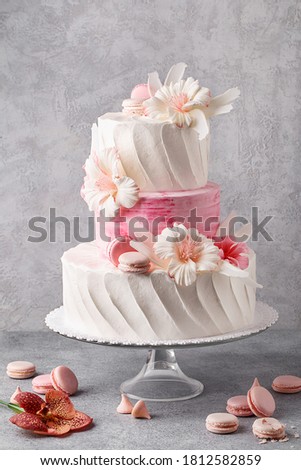 Tiered cake for wedding or birthday. Beautiful white and pink festive cake decorated with flowers and macaroons over gray concrete background. Side view