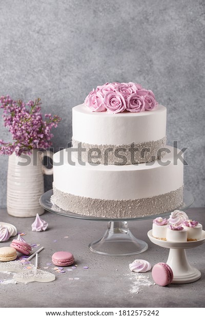 Tiered cake for wedding or\
birthday. Beautiful festive white cake decorated with cream roses\
and silver beads over gray concrete background. Side\
view