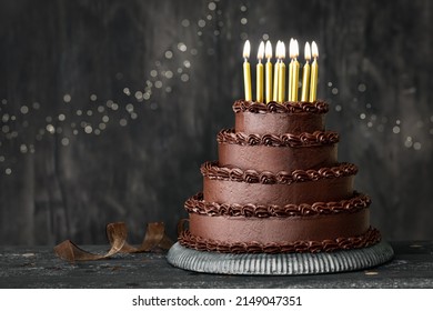 Tiered chocolate birthday cake decorated with chocolated frosting and gold birthday candles