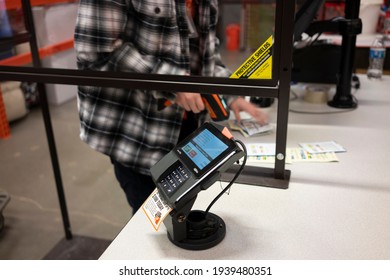Tigard, OR, USA - Mar 13, 2021: Closeup of the Ingenico Lane 7000 PIN pad in the checkout lane with a cashier in the background using a barcode scanner behind the screen in the Home Depot in Tigard.