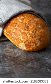 Tiger Loaf Of Bread Wrapped In A Grey Tea Towel. On A Black Stone Background